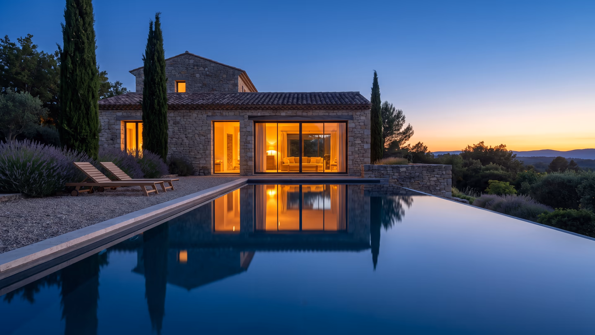 Maison en pierre du Sud de la France éclairée à la tombée de la nuit, reflétée dans sa piscine