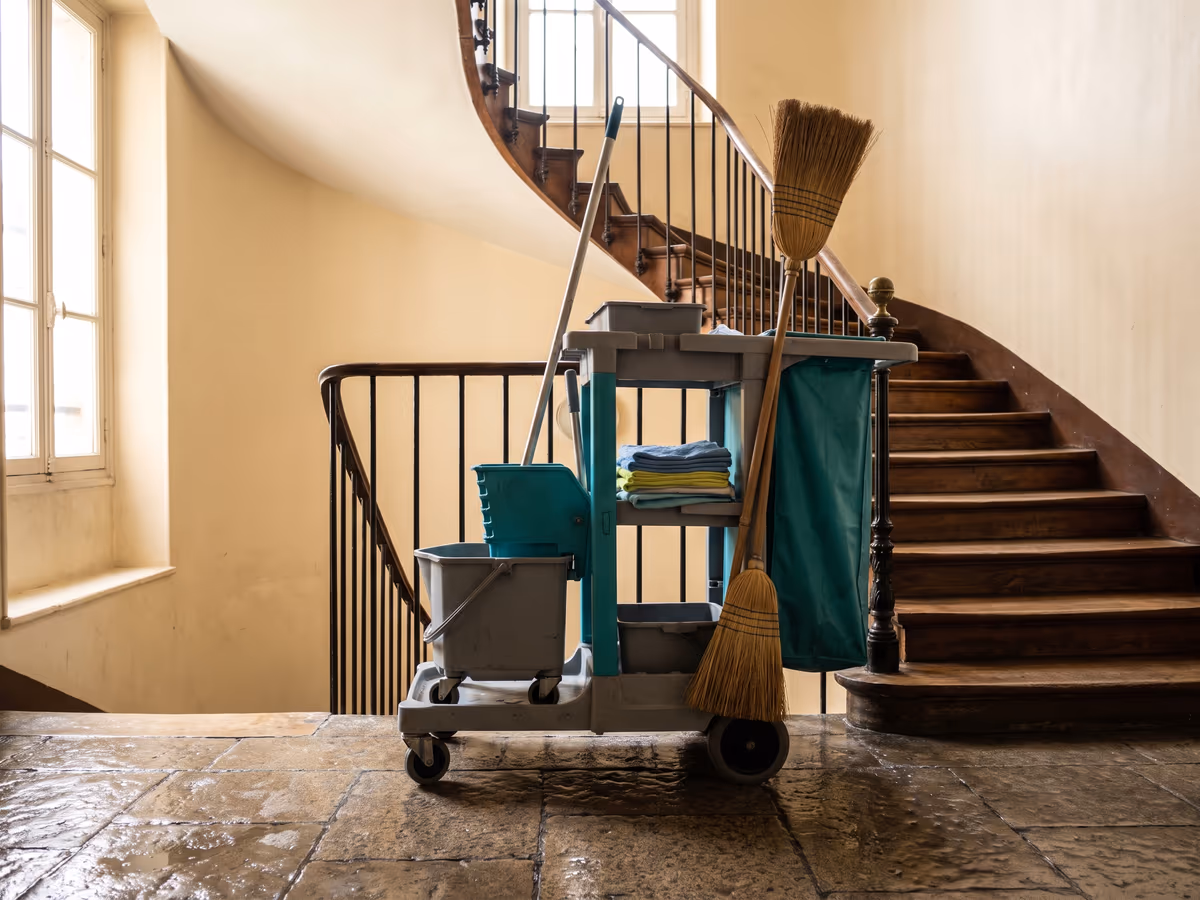 Chariot de ménage, seau et balais au pied d'un escalier d'immeuble