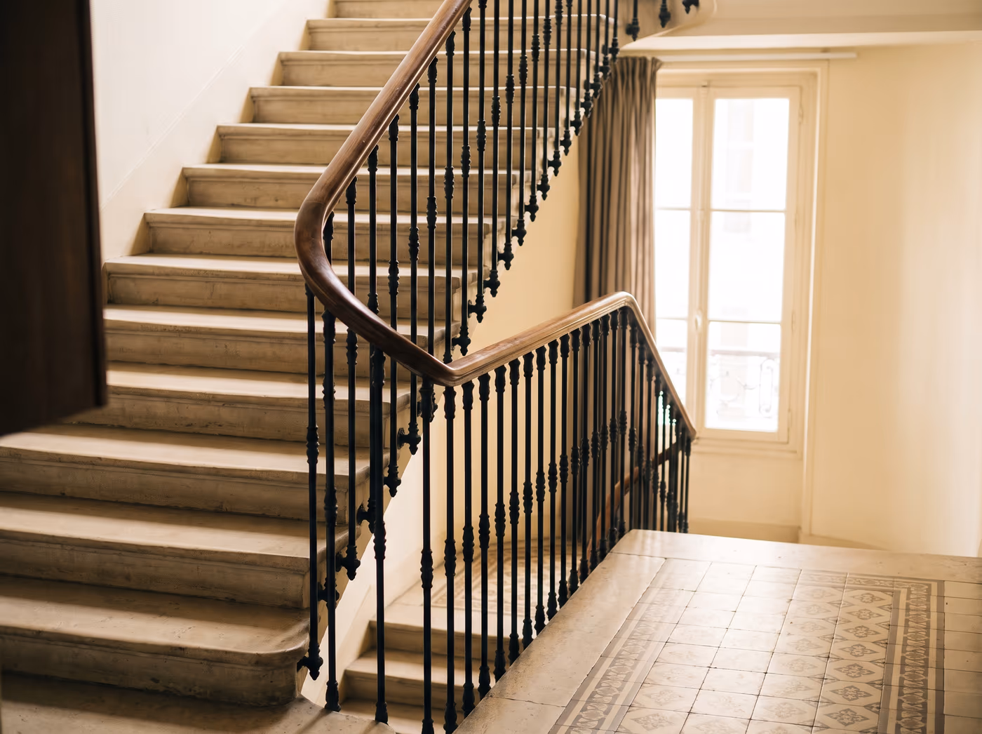 Cage d'escalier d'une copropriété : marches en pierre, rampe en bois et palier carrelé entretenus