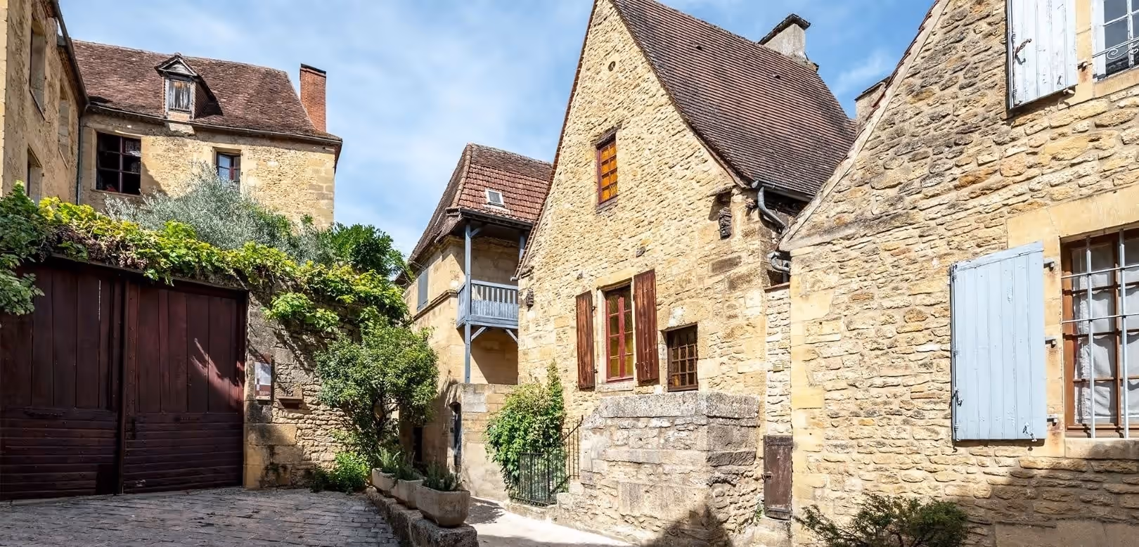 Le Petit Château, logement du réseau Hostcare à Sarlat-la-Canéda : une ruelle pavée bordée de maisons en pierre dorée aux volets bleus